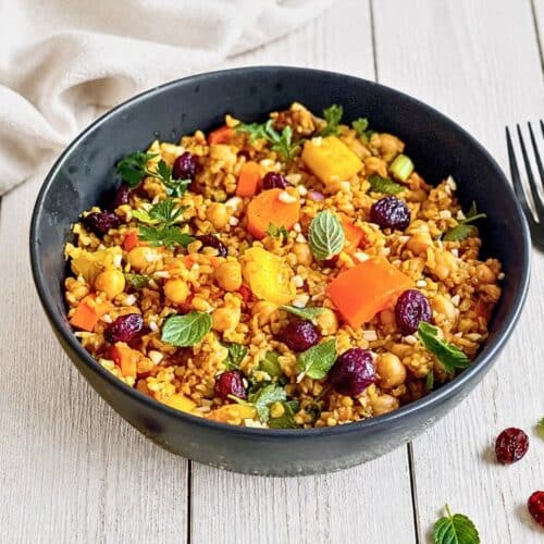 Veganer Bulgursalat mit Gemüse und Kräutern in einer Schüssel auf einem Holztisch.