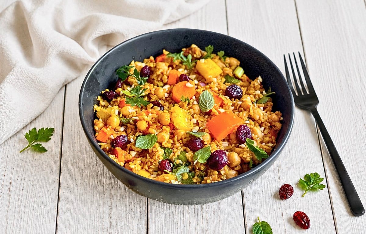 Veganer Bulgursalat mit Gemüse und Kräutern in einer Schüssel auf einem Holztisch.