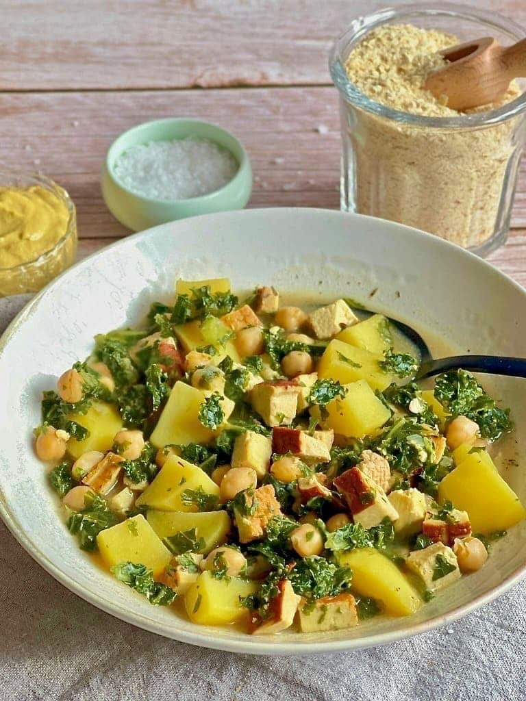 Veganer Kartoffel-Grünkohl-Eintopf mit Räuchertofu und Kichererbsen in einem Suppenteller.