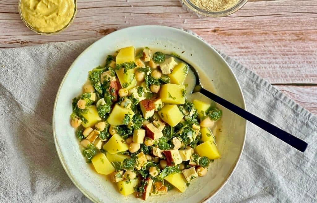 Veganer Kartoffel-Grünkohl-Eintopf mit Räuchertofu und Kichererbsen in einem Suppenteller.
