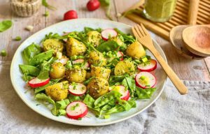 Veganer Kartoffelsalat mit Pesto, Rucola, Radieschen, Zuckerschoten und Frühlingszwiebeln auf einem Teller.