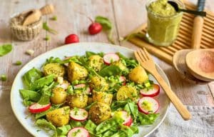 Veganer Kartoffelsalat mit Pesto, Rucola, Radieschen, Zuckerschoten und Frühlingszwiebeln auf einem Teller.