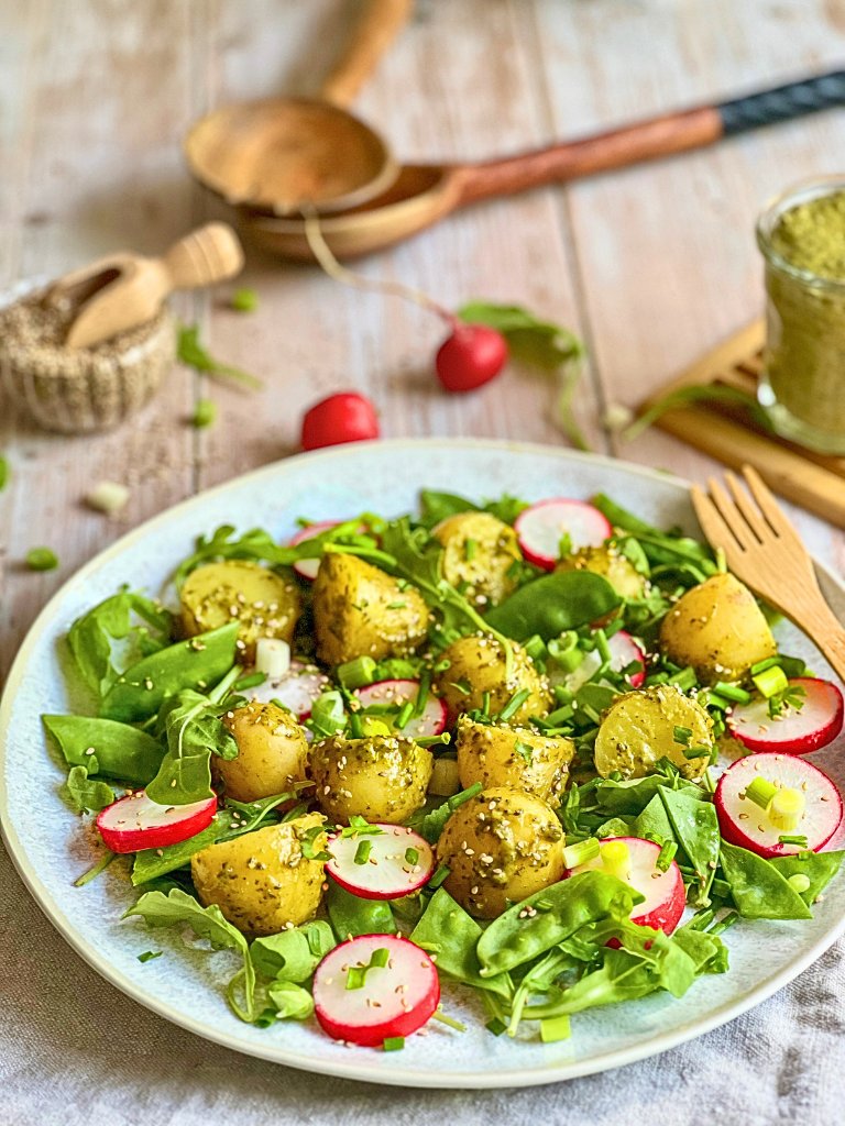 Veganer Kartoffelsalat mit Pesto, Rucola, Radieschen, Zuckerschoten und Frühlingszwiebeln auf einem Teller.