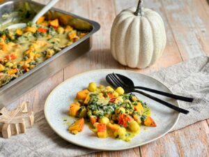 Veganer Kürbis-Gnocchi-Auflauf mit Käse überbacken auf einem Teller neben einer Auflaufform.