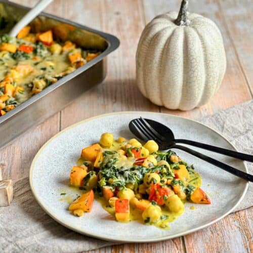 Veganer Kürbis-Gnocchi-Auflauf mit Käse überbacken auf einem Teller neben einer Auflaufform.