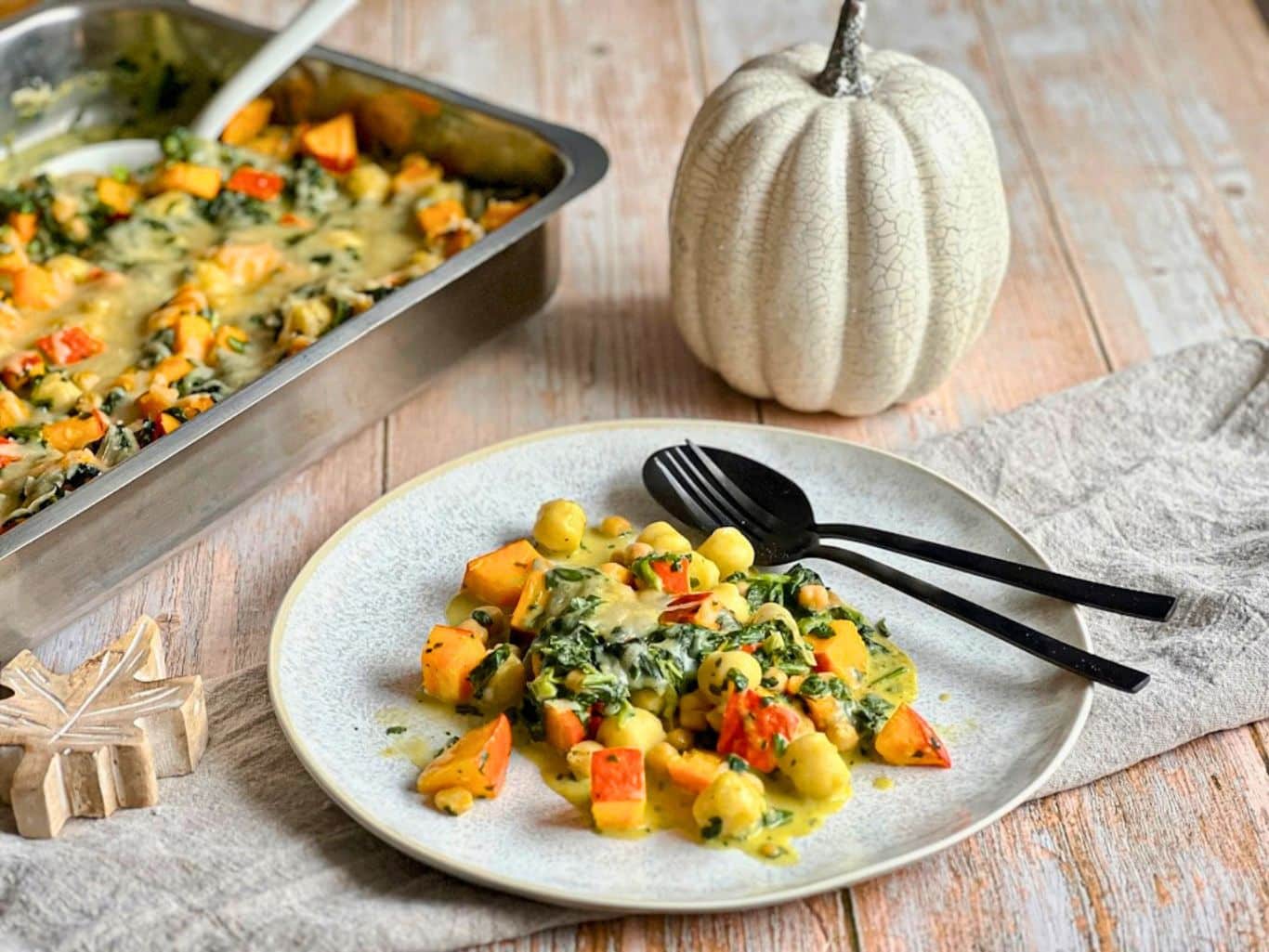 Veganer Kürbis-Gnocchi-Auflauf mit Käse überbacken auf einem Teller neben einer Auflaufform.