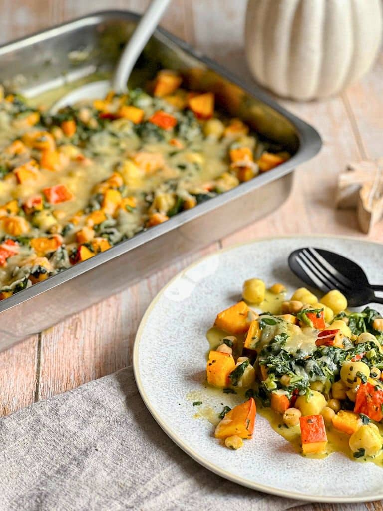 Leckerer veganer Kürbis-Gnocchi-Auflauf mit Käse überbacken auf einem Teller neben einer Auflaufform.