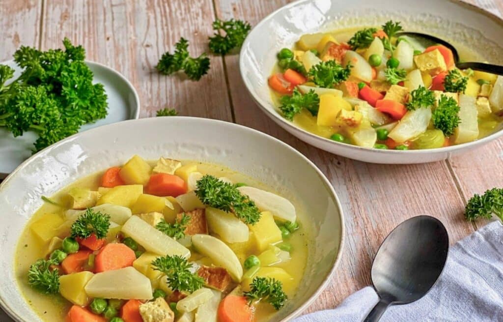 Veganer Mairübchen-Eintopf mit Gemüse, Kartoffeln, Räuchertofu und Petersilie in Suppentellern.