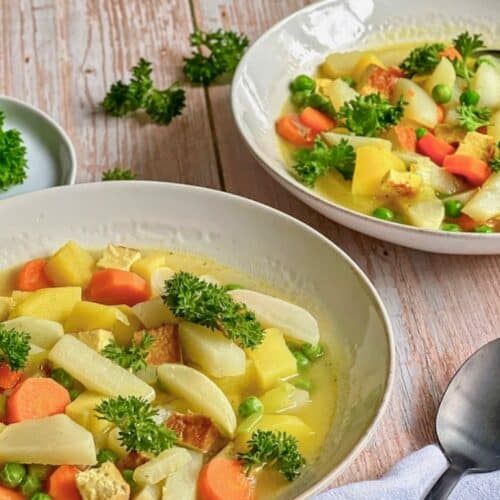 Veganer Mairübchen-Eintopf mit Gemüse, Kartoffeln, Räuchertofu und Petersilie in Suppentellern.