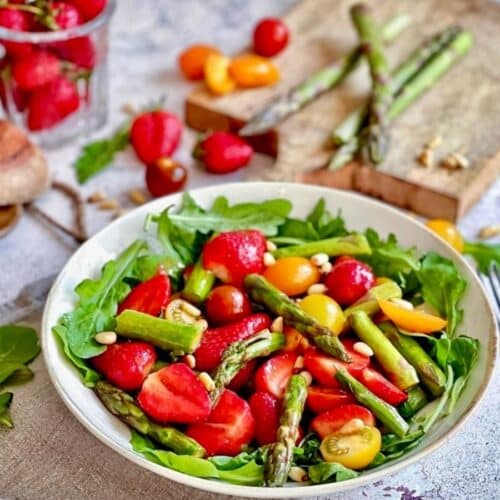 Veganer Spargelsalat mit Erdbeeren, Pinienkerne & Rucola auf einem Teller.