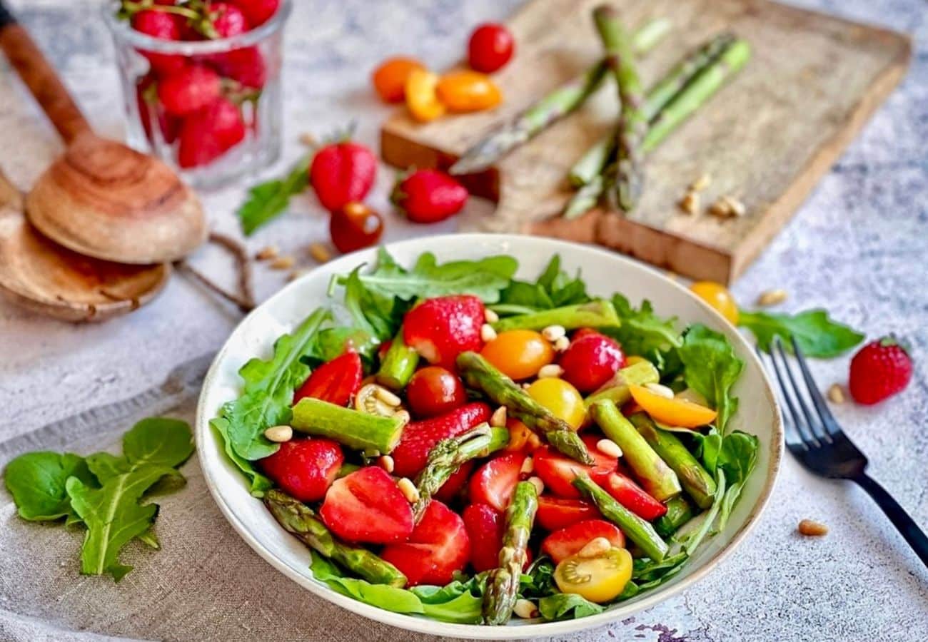 Veganer Spargelsalat mit Erdbeeren, Pinienkerne & Rucola auf einem Teller.