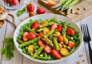 Veganer Spargelsalat mit Erdbeeren, Pinienkerne & Rucola auf einem Teller.