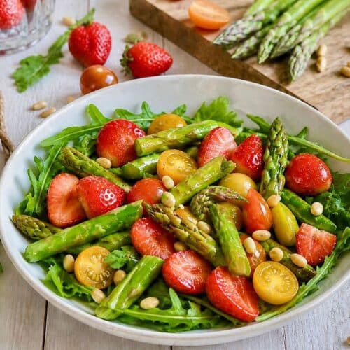 Veganer Spargelsalat mit Erdbeeren, Pinienkerne & Rucola auf einem Teller.