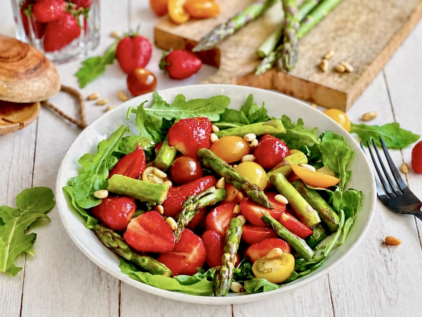 Veganer Spargelsalat mit Erdbeeren, Pinienkerne & Rucola auf einem Teller.
