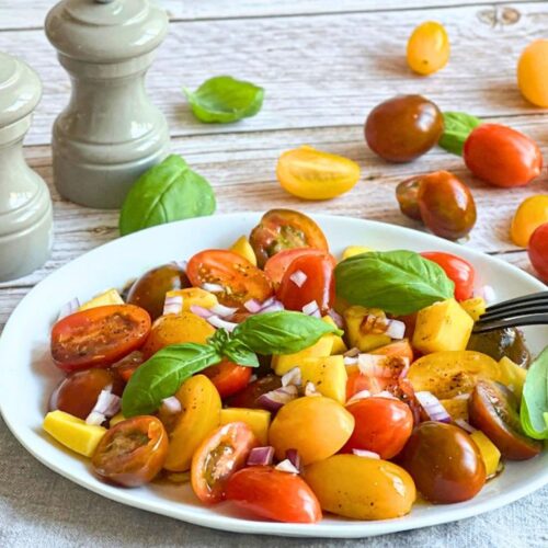 Veganer Tomaten-Mango-Salat mit Basilikum auf einem Teller.