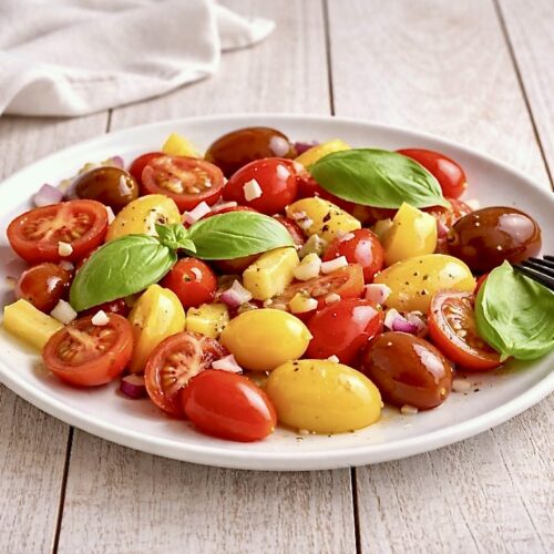 Tomaten-Mango-Salat mit Basilikum auf einem Teller.