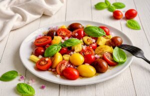 Veganer Tomaten-Mango-Salat mit Zwiebeln und Basilikum auf einem Teller.