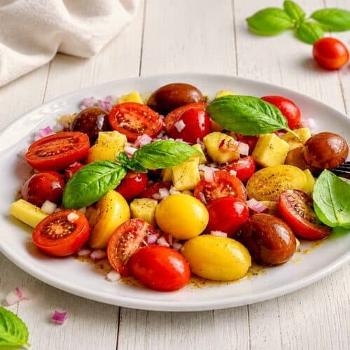 Veganer Tomaten-Mango-Salat mit Zwiebeln und Basilikum auf einem Teller.