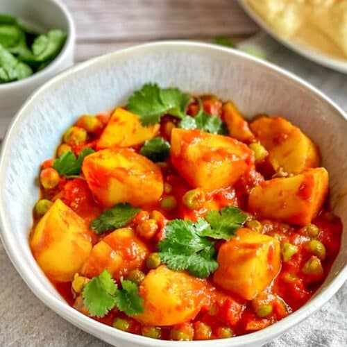 Aloo Matar: Ein herzhaftes indisches Curry mit Kartoffeln und Erbsen auf einem Teller mit Naan-Brot.