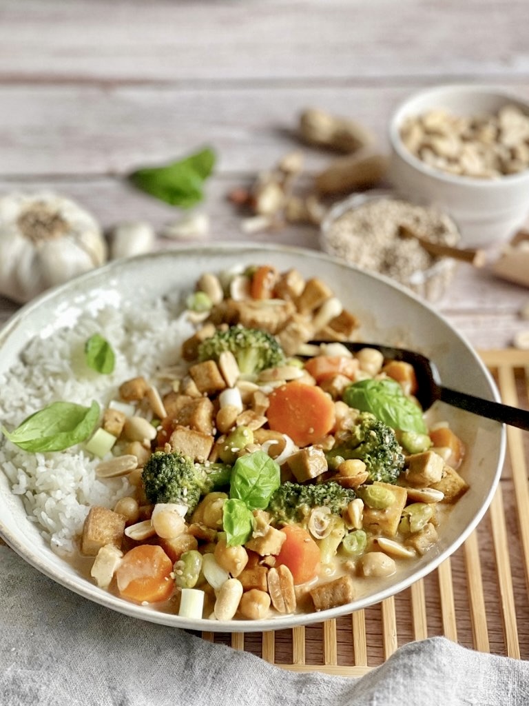 Gemüse mit Tofu in Erdnusssoße mit Reis auf einem Teller.