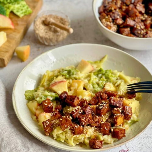 Veganes Wirsing-Risotto mit Räuchertofu, Äpfeln und Sesam auf einem Teller.