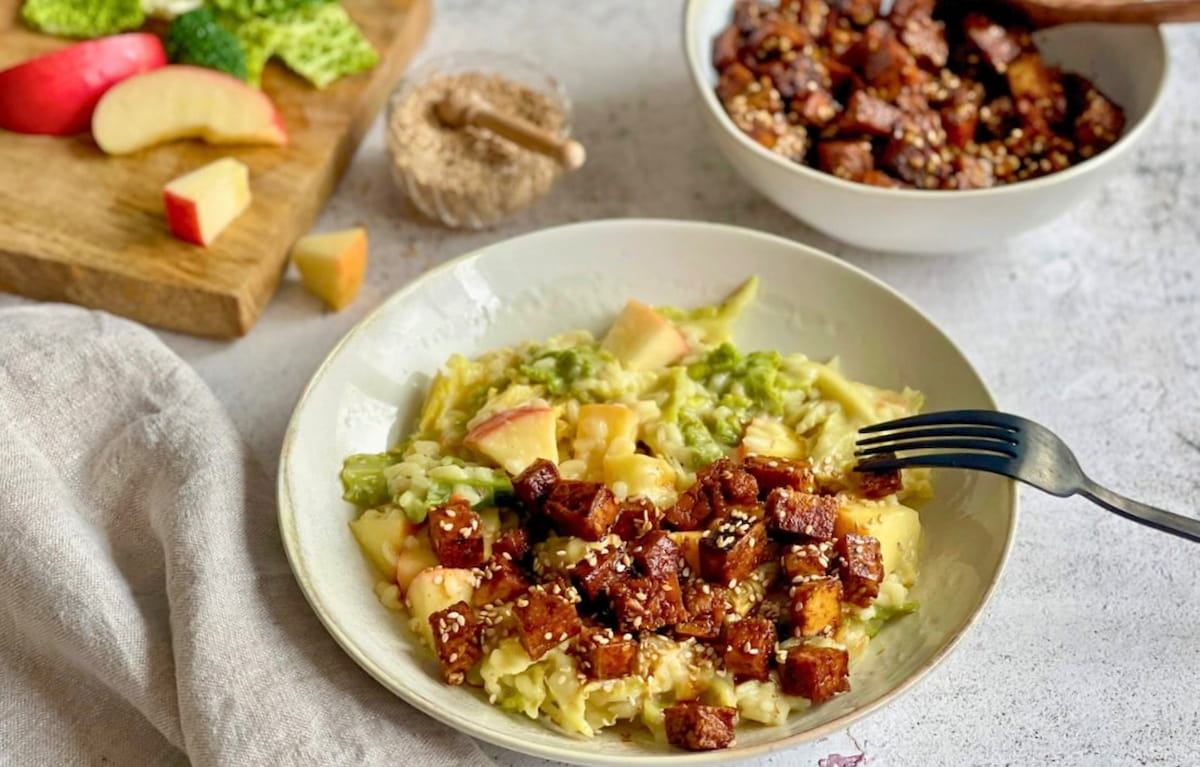 Veganes Wirsing-Risotto mit Räuchertofu, Äpfeln und Sesam auf einem Teller.