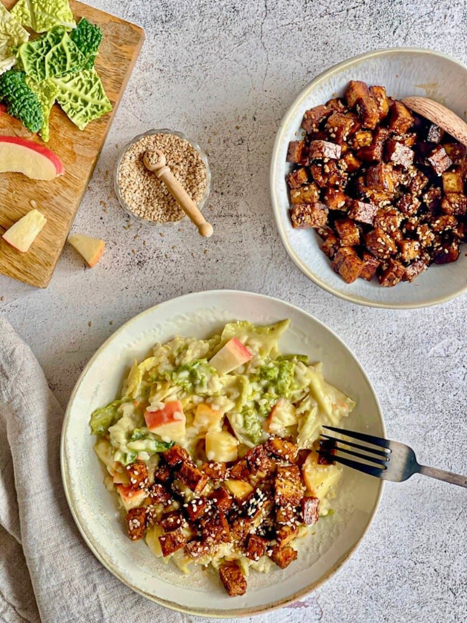 Veganes Wirsing-Risotto mit Räuchertofu, Äpfeln und Sesam auf einem Teller.