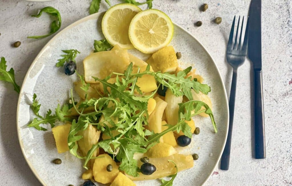 Zitroniges Fenchelgemüse mit Rucola, Kartoffeln, Kapern und Oliven auf einem Teller.