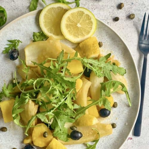 Zitroniges Fenchelgemüse mit Rucola, Kartoffeln, Kapern und Oliven auf einem Teller.