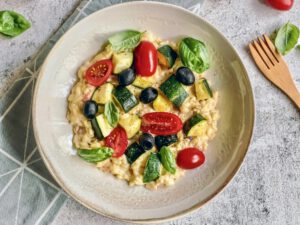 Veganes Zucchini-Risotto mit Tomaten, Oliven und Basilikum auf einem Teller.