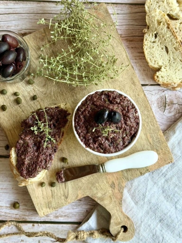 Vegane Oliventapenade auf einem Holzbrett.